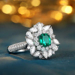 Load image into Gallery viewer, Ornate diamond ring featuring a central emerald surrounded by white gemstones in a floral design.
