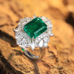 Load image into Gallery viewer, Emerald-cut green gemstone ring surrounded by diamonds in a white gold or platinum setting.
