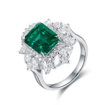 Load image into Gallery viewer, Emerald-cut green gemstone ring surrounded by diamond accents in a white metal setting.
