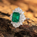 Load image into Gallery viewer, Emerald-cut green gemstone ring surrounded by diamonds in a white gold or platinum setting.
