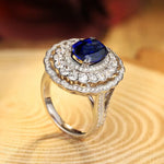 Load image into Gallery viewer, Ornate ring featuring a deep blue gemstone surrounded by diamonds in a double halo setting.
