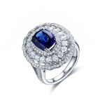 Load image into Gallery viewer, Ornate silver ring featuring a cushion-cut blue sapphire surrounded by diamonds.
