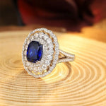 Load image into Gallery viewer, Ornate ring featuring a deep blue sapphire surrounded by diamonds in a double halo setting.
