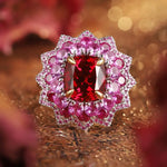 Load image into Gallery viewer, Ornate ring featuring a central red gemstone surrounded by pink and clear diamonds in a floral-inspired setting.
