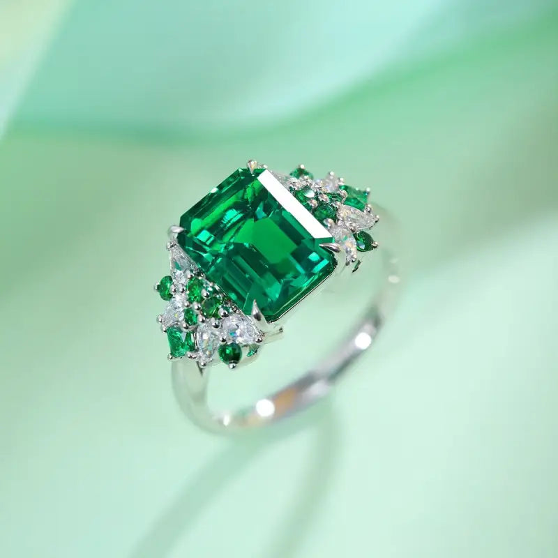 Emerald-cut green gemstone ring with diamond accents set in white metal.