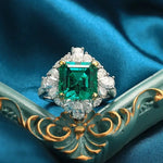 Load image into Gallery viewer, Ornate ring featuring a square-cut emerald surrounded by diamonds.
