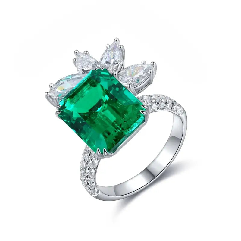 Emerald and diamond ring with a floral-inspired design set in white metal.