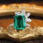 Load image into Gallery viewer, Emerald-cut green gemstone ring with diamond accents in a floral design.
