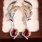 Load image into Gallery viewer, Ornate diamond and ruby earrings with feather-like designs and teardrop-shaped red gemstones.
