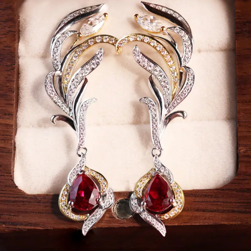 Ornate diamond and ruby earrings with feather-like designs and teardrop-shaped red gemstones.