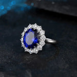 Load image into Gallery viewer, Ornate silver ring featuring a deep blue oval gemstone surrounded by smaller white stones.
