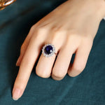 Load image into Gallery viewer, Ornate ring with a deep blue gemstone surrounded by smaller clear stones.
