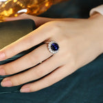 Load image into Gallery viewer, Ornate ring featuring a deep blue gemstone surrounded by smaller clear stones.
