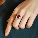 Load image into Gallery viewer, Ornate ring with a central red gemstone surrounded by smaller clear stones.
