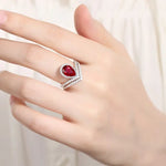 Load image into Gallery viewer, Elegant ring featuring a pear-shaped red gemstone surrounded by smaller clear stones in a curved design.
