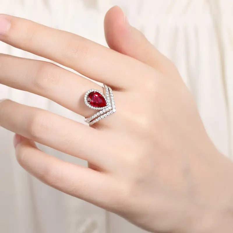 Elegant ring featuring a pear-shaped red gemstone surrounded by smaller clear stones in a curved design.