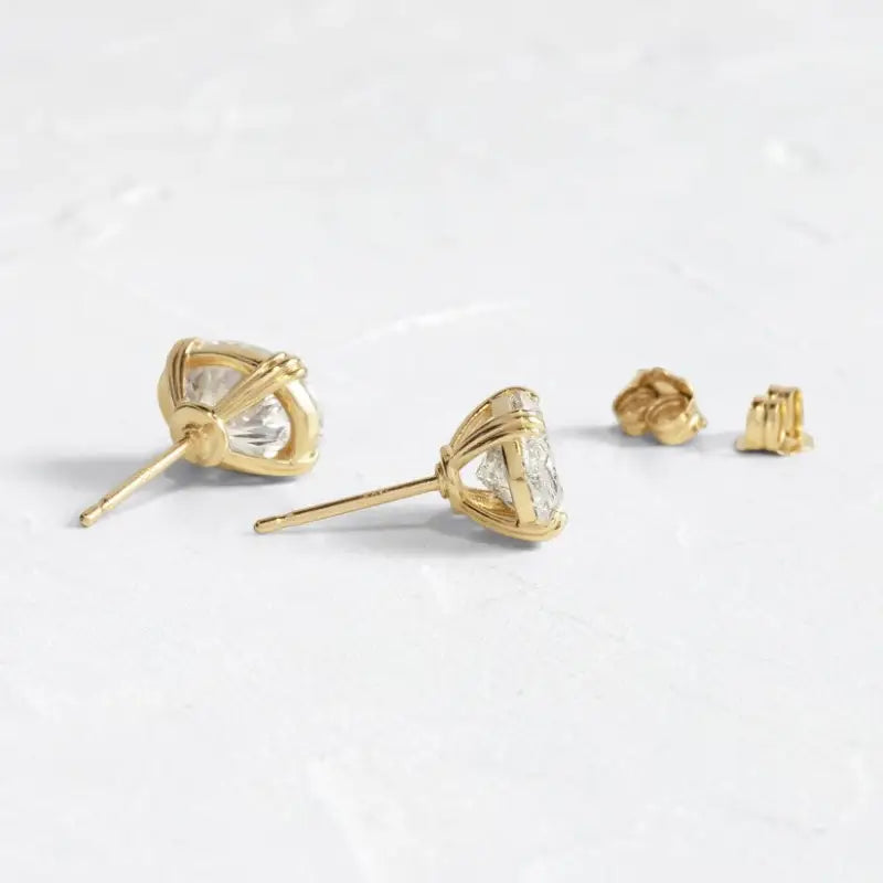 Gold stud earrings featuring heart-shaped prongs holding clear gemstones.