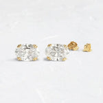 Load image into Gallery viewer, Pair of oval-cut diamond stud earrings set in gold prongs.
