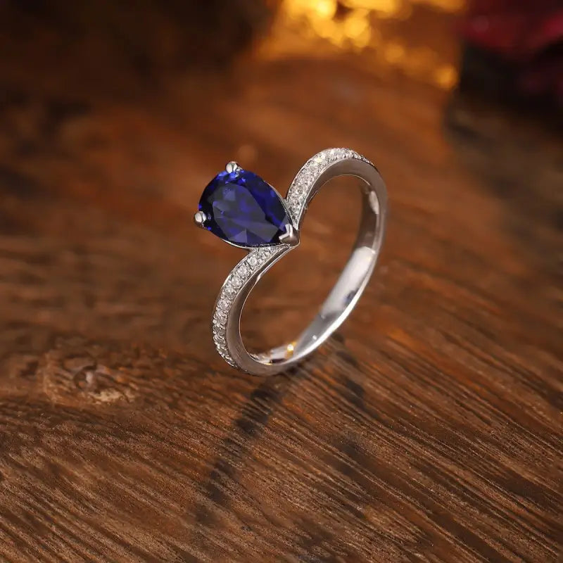 Elegant silver ring featuring a pear-shaped blue gemstone and small diamonds along the band.